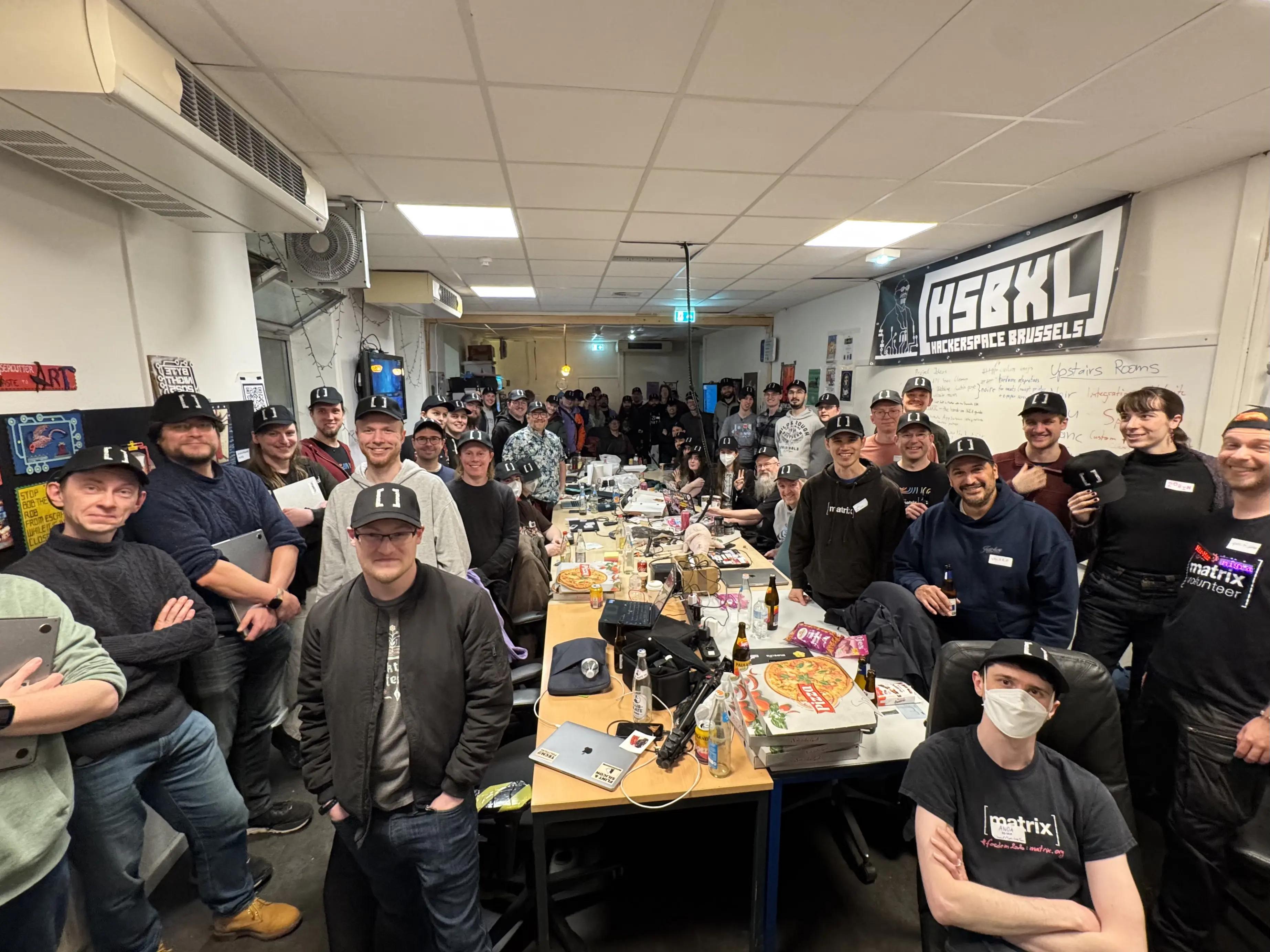 A picture of about a thousand people in a room, looking at the camera and smiling. All of them are wearing Matrix hats.